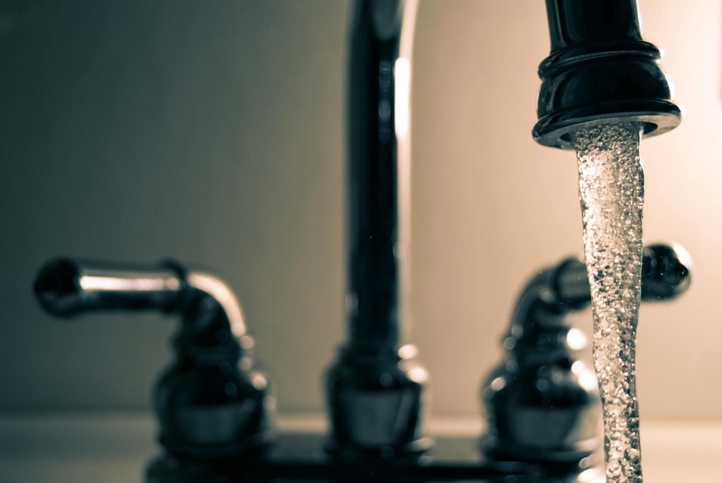 Ein Wasserhahn mit laufendem Wasser befindet sich in dunkler Umgebung